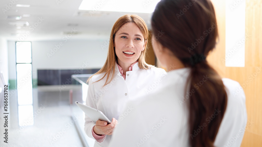 Young female scientist and her colleague chatting at the hallway of the hospital Young female scientist and her colleague chatting at the hallway of the hospital