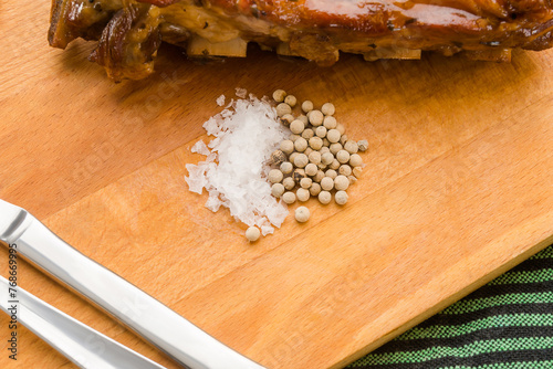 Pile of salt flakes and peppercorns on a wooden board.