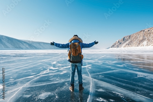 Man in winter hiking clothes with backpack stay on frozen icy lake with his arms spread to side. Tourism, freedom, trips. Generative AI © Elena