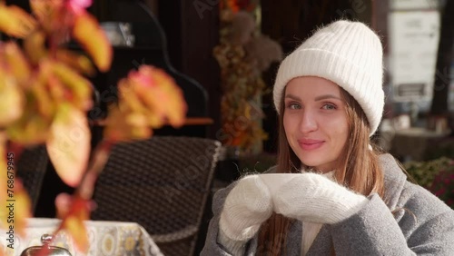 Attractive woman in warm white hat and mittens with cup of hot beverage outdoors on sunny autumn day photo