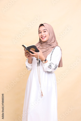 beautiful indonesia Muslim mature woman in hijab candid smiling at the camera holding prayer beads while reading the quran. for advertising, lifestyle, banners and Ramadan