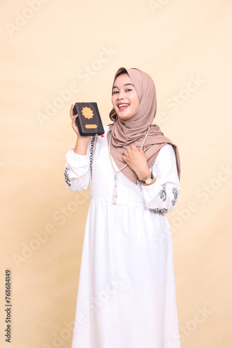 The beauty of a young Asian Muslim woman wearing a hijab, smiling cheerfully, holding a quran and wearing a prayer beads necklace. for advertising, lifestyle, banners and Ramadan
