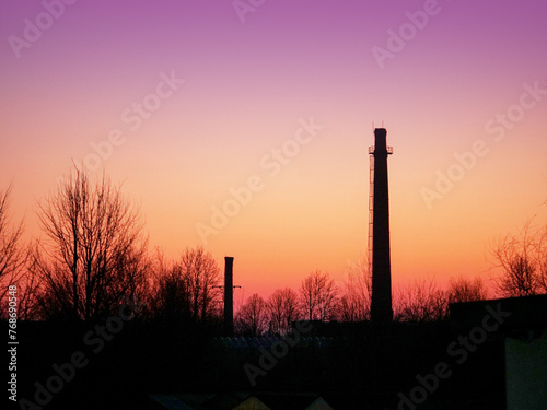 Silhouette of a tall factory chimney against red and purple sunrise sky. No smoke. Commercial industrial object. Nobody.