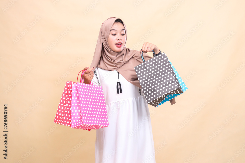 the charm of a young Asian Muslim woman wearing a hijab is surprised to the left looking at and carrying the contents of a colorful paper bag from shopping from top to bottom the charm of a young Asian Muslim woman wearing a hijab is surprised to the left looking at and carrying the contents of a colorful paper bag from shopping from top to bottom