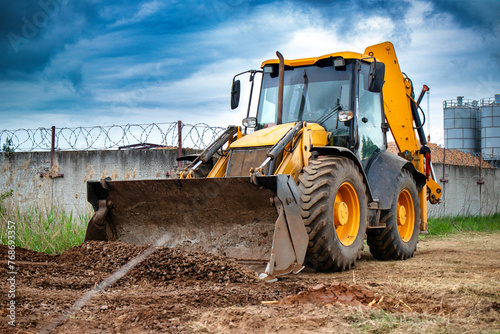 A bulldozer or a loader is actively digging dirt in front of a sturdy barbed wire fence, showcasing industrial activity and security measures