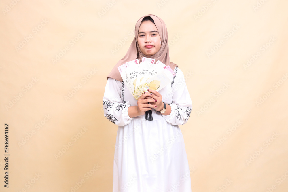 portrait of a beautiful indonesia Muslim woman wearing a hijab, sullen and disappointed, holding a gift or fitrah on Eid. used for advertising, giveaways, Eid and Ramadan portrait of a beautiful indonesia Muslim woman wearing a hijab, sullen and disappointed, holding a gift or fitrah on Eid. used for advertising, giveaways, Eid and Ramadan