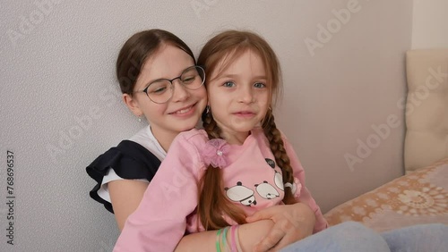 glasses, holds a younger sister of preschool age in her arms, the children smile and look into the frame, calm happy children. International Sibling Day.