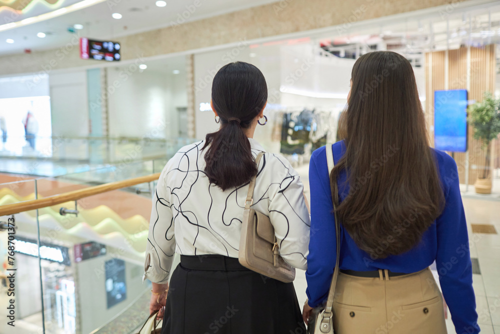 Back view of two women walking in mall and looking at window displays while enjoying shopping together copy space Back view of two women walking in mall and looking at window displays while enjoying shopping together copy space