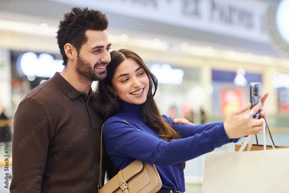 Side view portrait of happy couple taking selfie photo in shopping mall while enjoying date together copy space