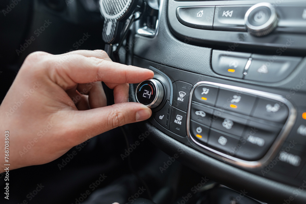 Man's hand turns the climate control wheel in a car. Temperature setting