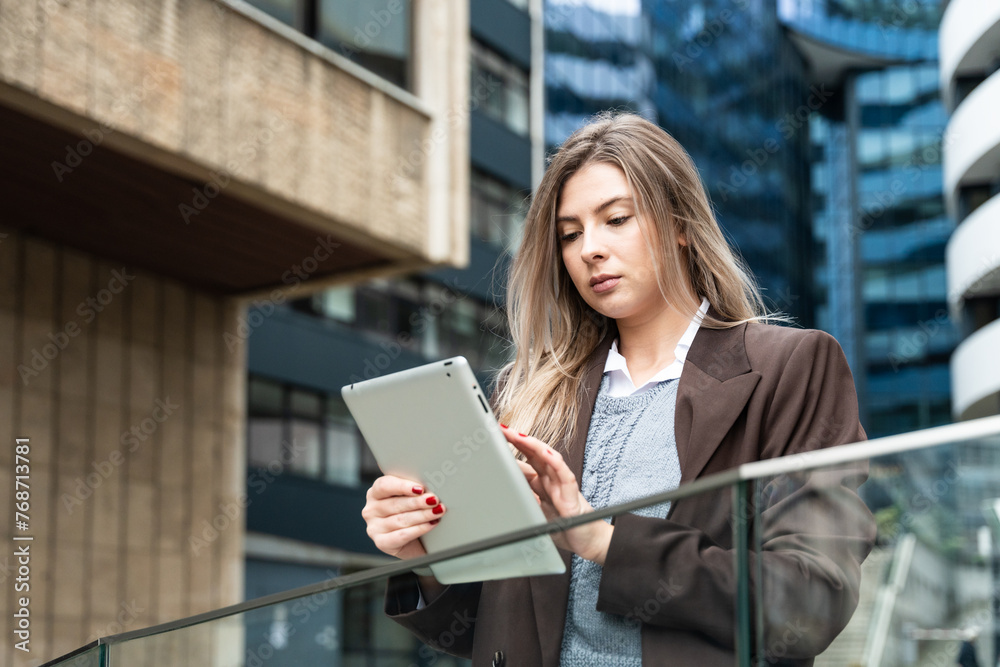 Portrait of a successful business woman using digital tablet in front of modern business office building. Professional female, financial expert, project leader and staff manager standing outdoor Portrait of a successful business woman using digital tablet in front of modern business office building. Professional female, financial expert, project leader and staff manager standing outdoor