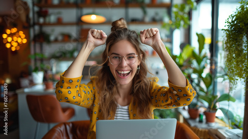 Joyful young woman celebrating success in a cozy cafe with a laptop