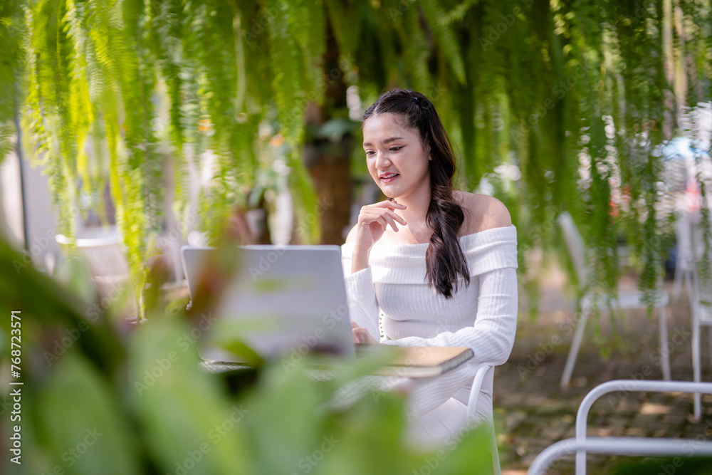 A happy young woman enjoys remote work on her laptop, comfortably seated outdoor of cafe with a coffee. A happy young woman enjoys remote work on her laptop, comfortably seated outdoor of cafe with a coffee.