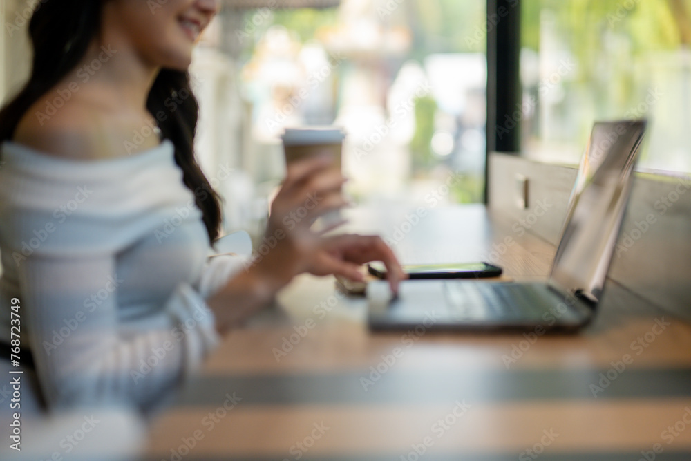 An out-of-focus shot captures a young woman in a casual setting, sipping coffee while working on a laptop, conveying a relaxed atmosphere. An out-of-focus shot captures a young woman in a casual setting, sipping coffee while working on a laptop, conveying a relaxed atmosphere.