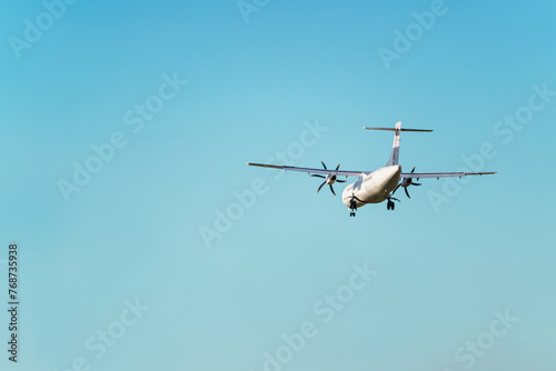 Rear view of an ATR 72 airplane, a twin-engine turboprop short-haul regional passenger aircraft. Landing airplane. Blue background. Clear sky.