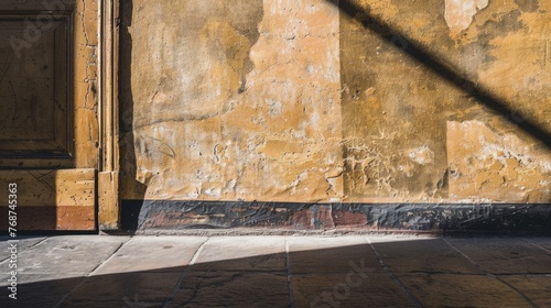 Afternoon sunlight casts a diagonal shadow over the textured surface of an orange wall meeting a stone pavement.