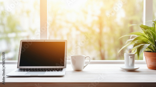 Laptop and coffee cup on wooden table in front of window with sunlight .