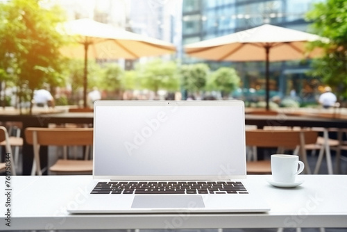 Laptop with blank screen and coffee cup on table in outdoor cafe