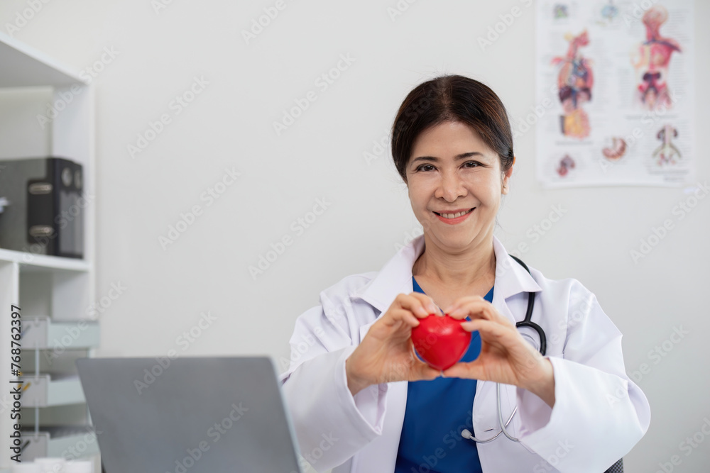 Happy young doctor senior woman holding red heart shape object, looking at camera with smile. Positive practitioner, cardiologist