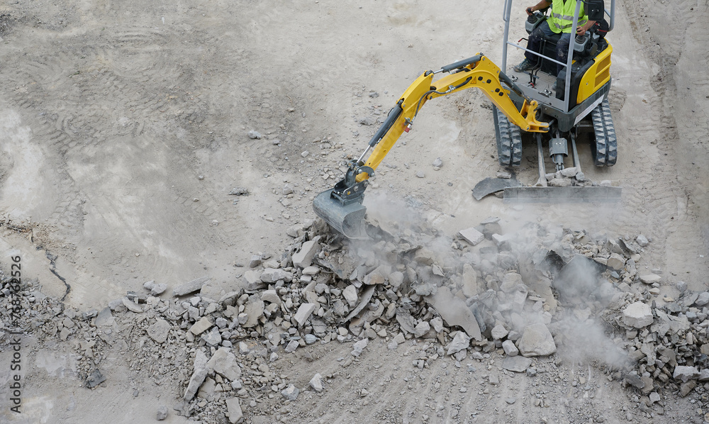 Worker operates a mini excavator to remove old concrete at the ground renovation work at the construction site. - obrazy, fototapety, plakaty 