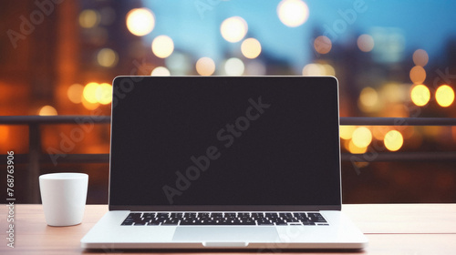 Laptop with blank screen on wooden table in front of blurred city lights background