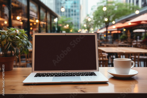 Laptop with blank screen and coffee cup on table in coffee shop