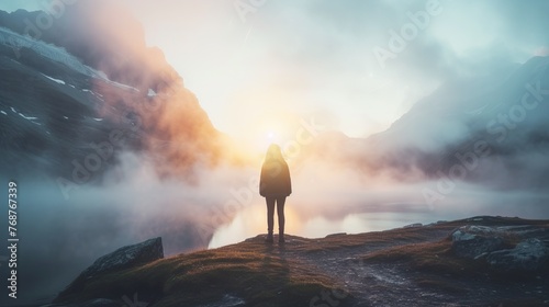 Silhouette of a person standing on a mountain peak with dramatic sunrise clouds in the background. photo
