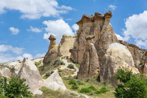 Unique fairy chimneys in Cappadocia under a blue sky, with greenery accentuating their ancient, sculpted forms. Cavusin, Avanos, Turkiye (Turkey)