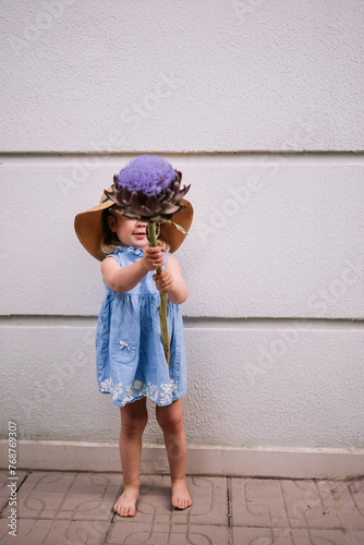 Cute little girl holding big artichoke flower in hands