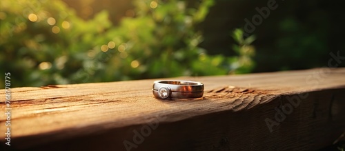 A gold wedding ring is delicately placed on a weathered wooden bench, basking in the warm sunlight