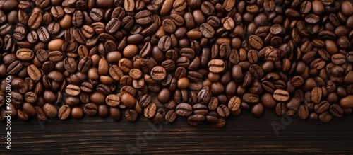 Many coffee beans in a heap spread out on a rustic wooden surface © vxnaghiyev