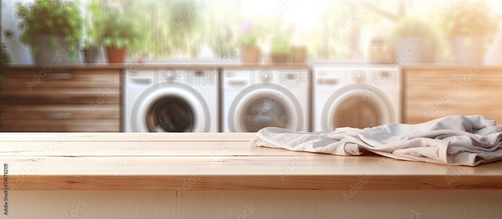 A wooden table covered with a cloth is positioned in front of a washing machine, with laundry in the background