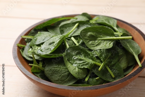 Fresh spinach leaves in bowl on light wooden table, closeup
