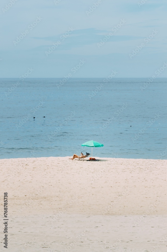 Young woman relaxing on a chair on a sunny beach day, sheltered by an umbrella for shade