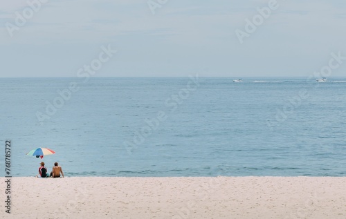 two people sitting under an umbrella at the beach by the water
