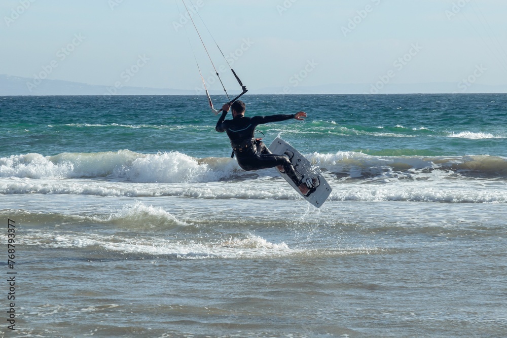 Hispanic young man doing kitesurfing with foamy waves in Tarifa, Spain on a sunny day