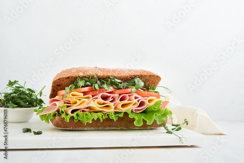 Sandwich. One fresh big submarine sandwich with ham, cheese, lettuce, tomatoes and microgreens on light background. Healthy breakfast theme concept, school lunch, breakfast or snack.