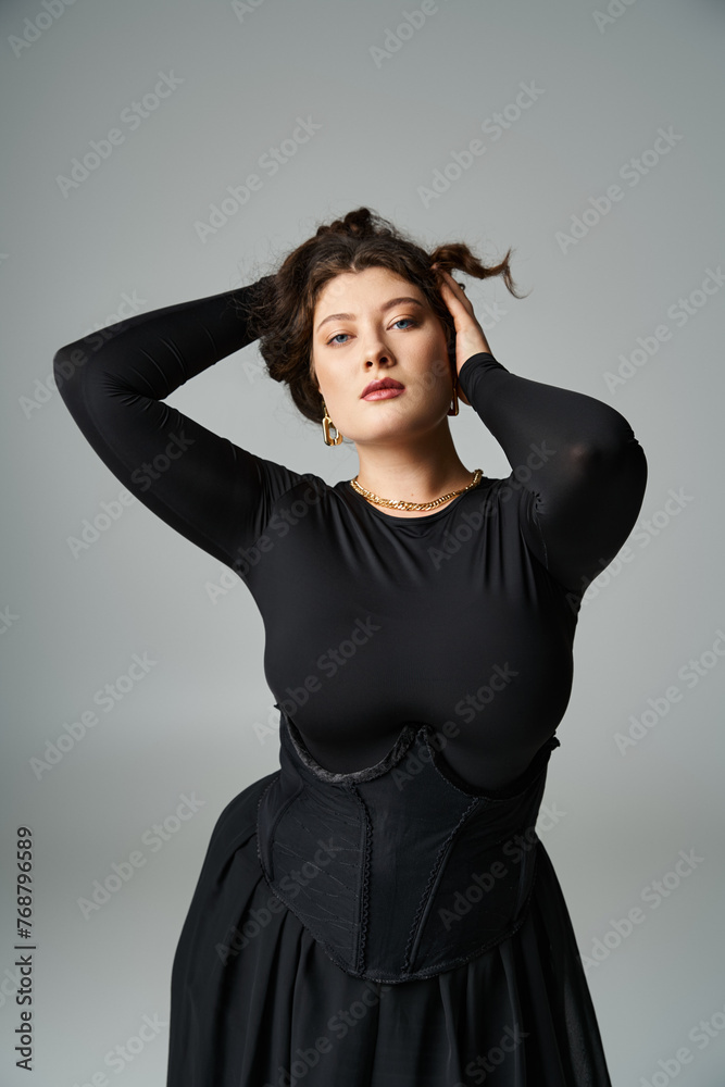 alluring plus size girl in her 20s putting hands behind head and holding hair on grey background