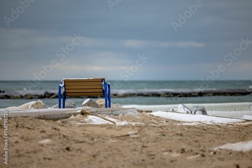 Wooden bench is situated on a beach with some ice nearby