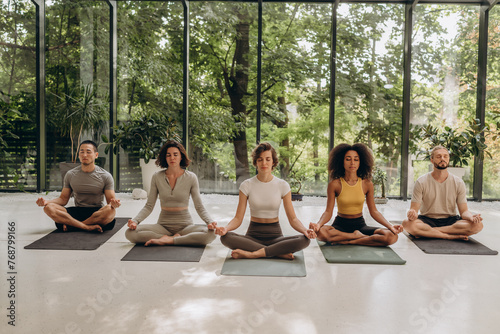 Group of people sitting in lotus pose on yoga mats in studio