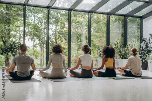 People meditating near panoramic windows with forest view 