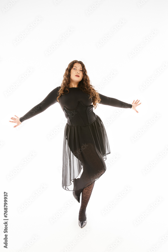beautiful curvy young woman in black stylish outfit with curly hair posing with hands on sideways