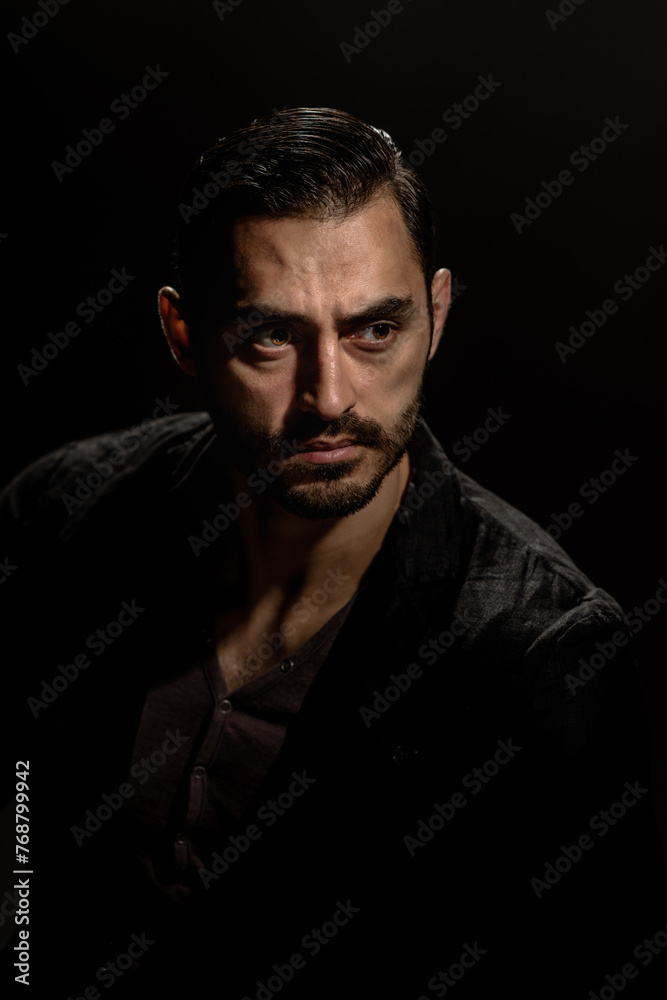 Fototapeta premium Portrait of young fashionable bearded man isolated on black background, Dramatic low-key portrait of a young man with a dark ambiance, showcasing his beard