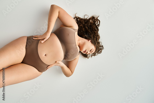 plus size young girl in brown underwear with hands on waist and closed eyes leaning head © LIGHTFIELD STUDIOS