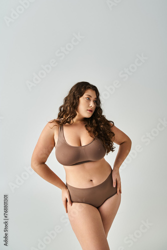 charming curvy girl in brown underwear with curly hair posing hands on hips and looking to side © LIGHTFIELD STUDIOS