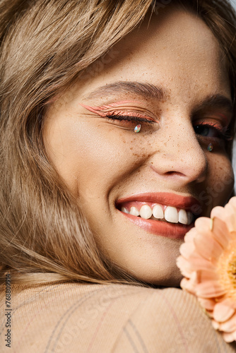Closeup beauty shot of woman winking with peach makeup  gerbera daisy  face jewels and freckles