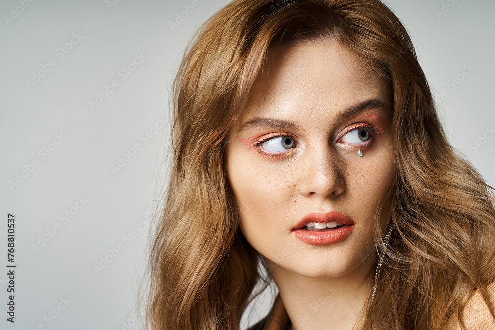 Naklejka premium Closeup portrait of woman with tear face jewels, peach makeup and freckles looking away