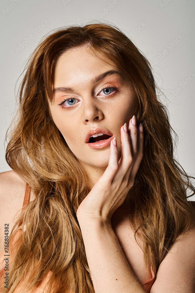 Peach fuzz. Attractive surprised woman with blue eyes, touching her cheek on grey background Peach fuzz. Attractive surprised woman with blue eyes, touching her cheek on grey background
