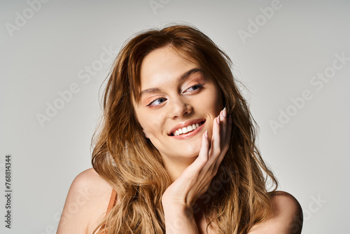 Attractive smiling woman with blue eyes, touching her cheek posing on grey background