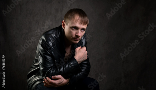 Serious man in a leather jacket looks to the side on a dark abstract background. A thoughtful and confident person. Dramatic photo.